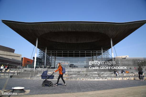 Woman pushes a pram past the Senedd Building in Cardiff Bay, south Wales on March 24, 2020 after Britain's government ordered a lockdown to slow the...