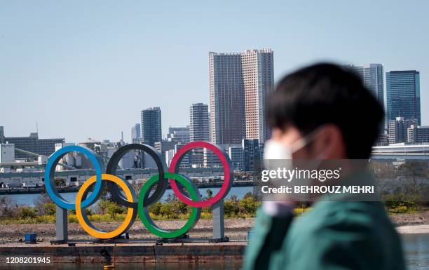 Man wearing a face mask, amid concerns over the spread of the COVID-19 novel coronavirus, stands before the Olympic rings from an observation point...