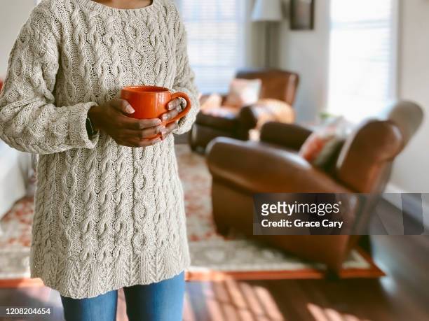 close-up of woman standing in living room holding coffee mug - pantaloni arancioni foto e immagini stock
