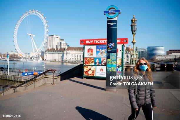 Woman wears a mask as she walks on Westminster Pier with the London Eye in the backgroud, in a near deserted central London on March 25 after...