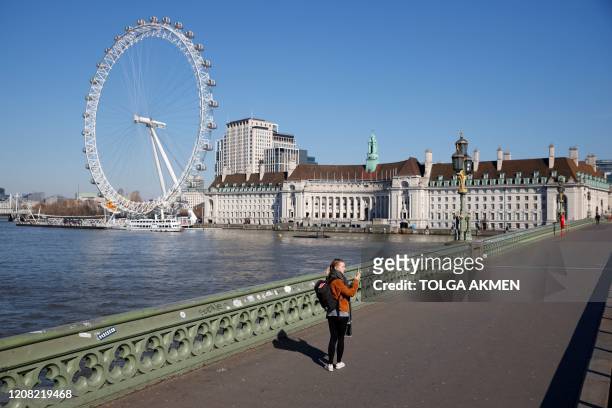 Woman takes photos as she walks on Westminster Bridge with the London Eye in the backgroud, in a near deserted central London on March 25 after...