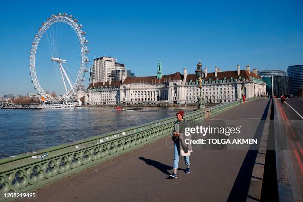 Woman walks on Westminster Bridge with the London Eye in the backgroud, in a near deserted central London on March 25 after Britain's government...