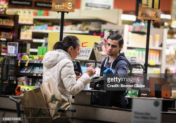 Cashier wears gloves while scanning the groceries of a customer at a Whole Foods in Cambridge, MA on March 24, 2020. Grocery stores have become even...