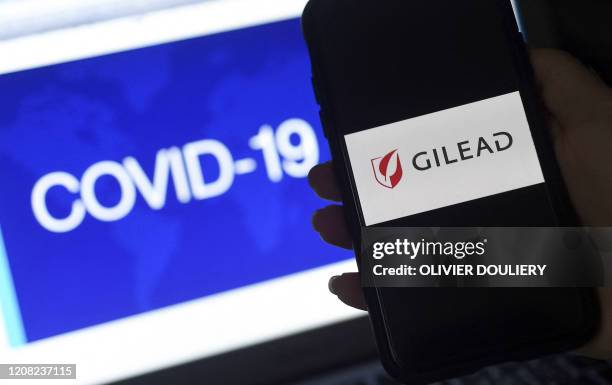 In this photo illustration a Gilead logo is displayed on a smartphone next to a screen showing a COVID-19 graphic on March 25, 2020 in Arlington,...