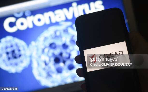 In this photo illustration a Gilead logo is displayed on a smartphone next to a screen showing a coronavirus graphic on March 25, 2020 in Arlington,...