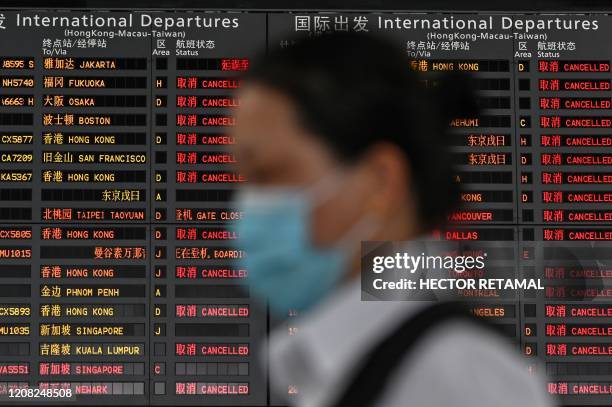 Woman wearing a facemask as a preventive measure against the COVID-19 novel coronavirus walks in front of a screen showing international departures...