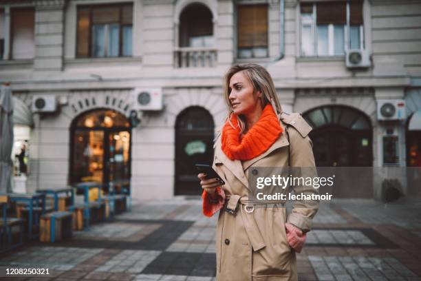 donna alla moda che controlla le app sul suo smartphone - trench foto e immagini stock