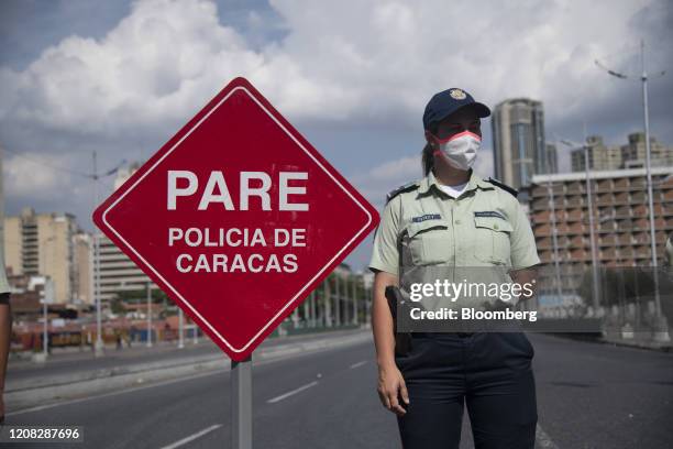 Member of the Bolivarian National Police wearing a protective mask stands guard on Bolivar Avenue in downtown Caracas, Venezuela, on Thursday, March...