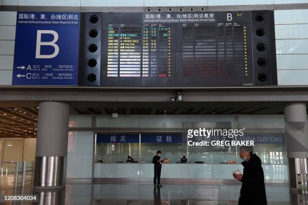 People stand below a board showing interenational arrivals in the empty arrivals area in Beijing Capital Airport on March 27, 2020. - China will...