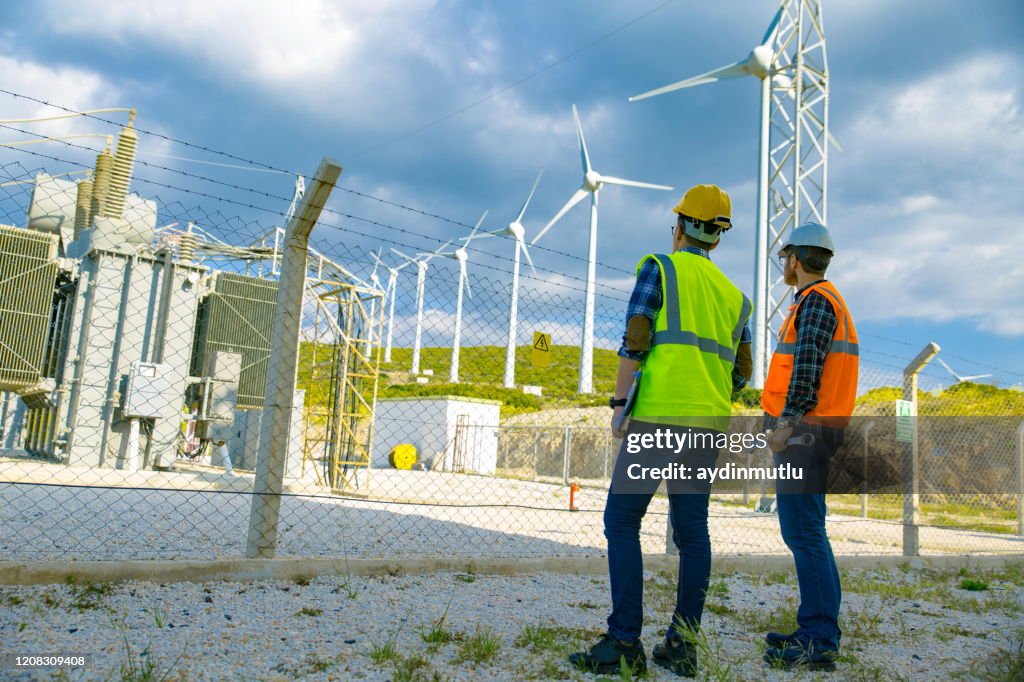 Young workers looking and checking wind turbines at field