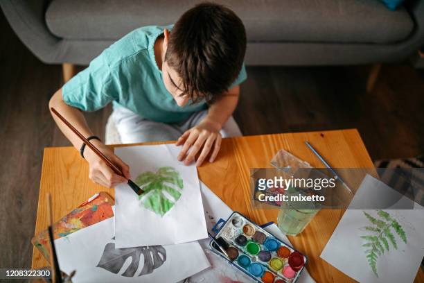 teenage boy watercolor painting while sitting on floor in living room - 12 year old cute boys stock pictures, royalty-free photos & images