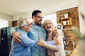 Cheerful senior couple and their adult son having fun while embracing at home.
