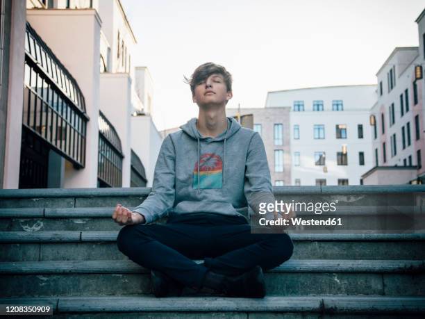 teenager sitting on steps meditating in the city - lotussitz stock-fotos und bilder