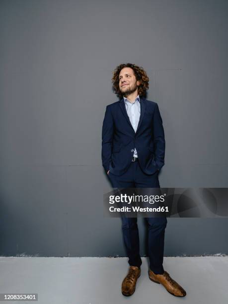 smiling businessman standing in front of gey wall - gelassene person stock-fotos und bilder