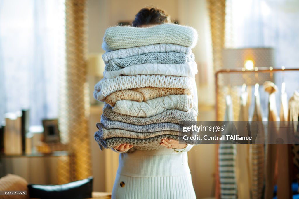 Woman in modern house in sunny winter day holding huge sweaters