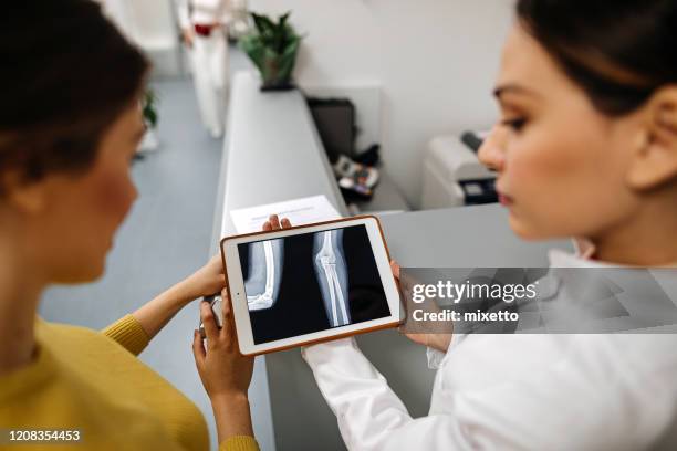 female doctor showing to patient x-ray image using digital tablet at medical clinic - doctor looking over shoulder stock pictures, royalty-free photos & images