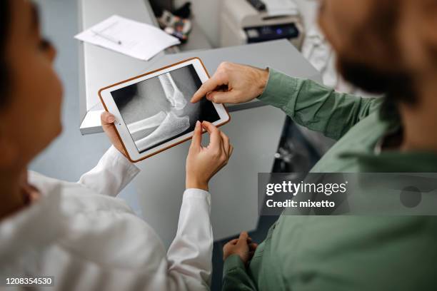 female doctor showing to patient x-ray image using digital tablet at medical clinic - broken trust stock pictures, royalty-free photos & images