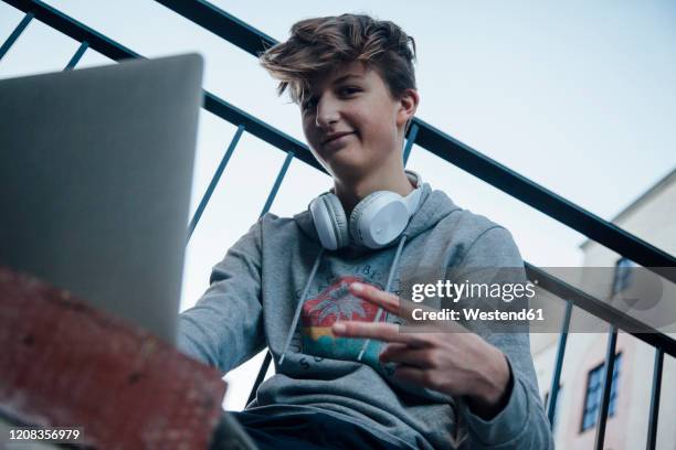 teenager using laptop in the city, showing victory sign - hoodie headphones - fotografias e filmes do acervo