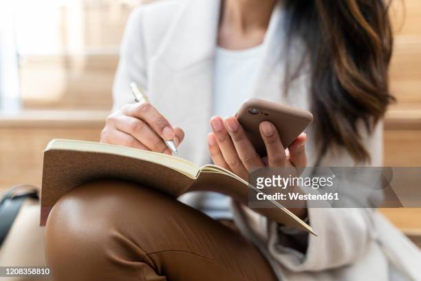 close-up of woman sitting on stairs using smartphone and taking notes - leather pants stockfoto's en -beelden