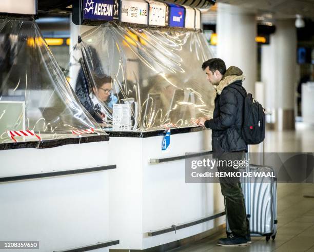 Passenger stands at an airline counter protected with a plastic tarpaulin on March 27, 2020 at the Amsterdam Schiphol airport which operates on lower...