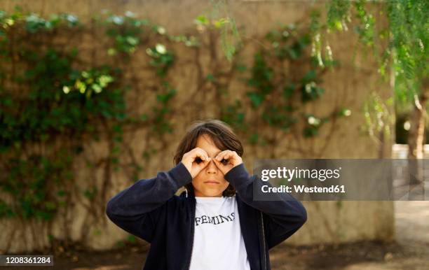 little boy looking through fingers,  with print on t-shirt, saying feminist - child with binoculas stockfoto's en -beelden