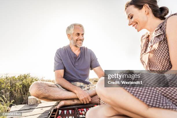 happy couple sitting on boardwalk at the coast playing backgammon - backgammon stockfoto's en -beelden