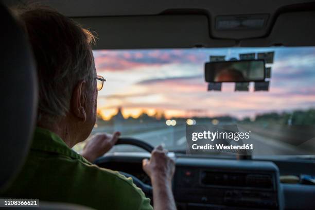 senior man driving a car on a highway at sunset - lenkrad stock-fotos und bilder