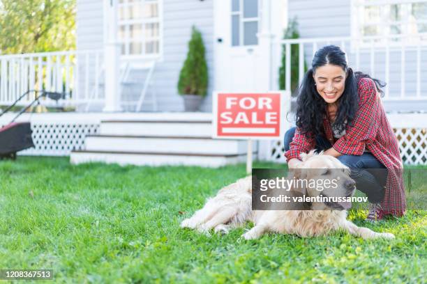smiling woman in front of "for sale" sign, kneeling next to golden retriever - home sweet home dog stock pictures, royalty-free photos & images
