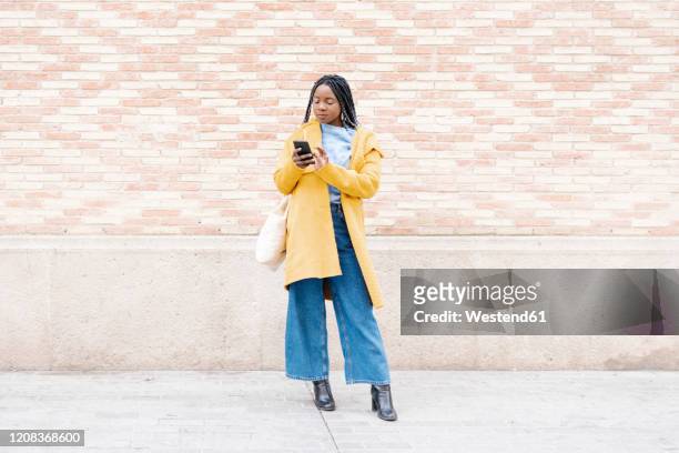 portrait of young woman standing on pavement looking at cell phone - woman jeans stock pictures, royalty-free photos & images