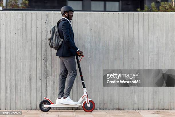 smiling businessman on push scooter in front of concrete wall - man on scooter stock pictures, royalty-free photos & images