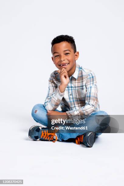 portrait of happy boy sitting against white background - auf dem boden sitzen stock-fotos und bilder