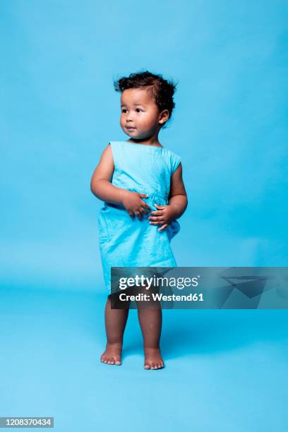 portrait of barefoot little girl wearing light blue dress standing against blue background - little black dress - fotografias e filmes do acervo