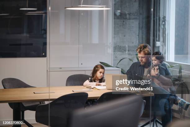 casual businessman with two daughters working at desk in office - kid office stock-fotos und bilder