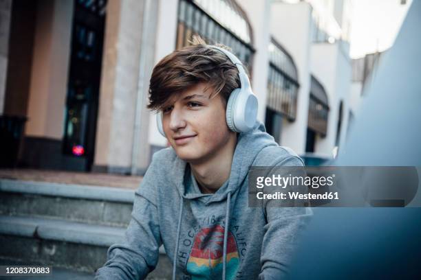 portrait of teenager with headphones, sitting on steps in the city - boy headphones stock-fotos und bilder