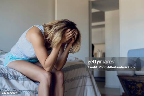 stressed woman sitting on bed - triste photos et images de collection