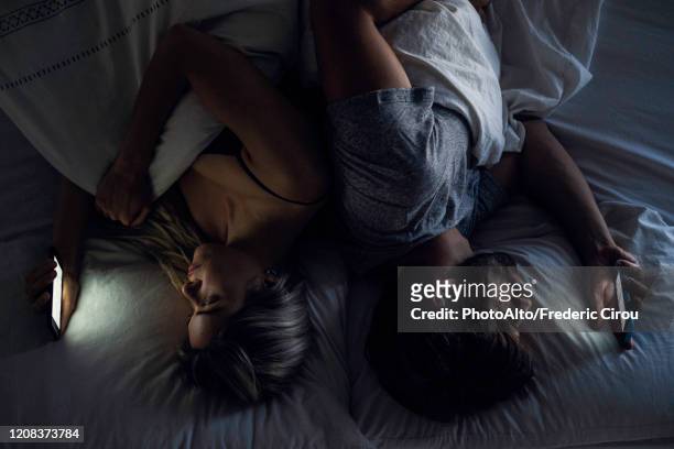 young couple using smartphones on bed - couple smartphone stockfoto's en -beelden