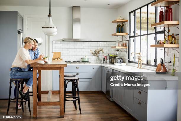 souriant couple à l'aide d'un ordinateur portable dans la cuisine - tabouret photos et images de collection