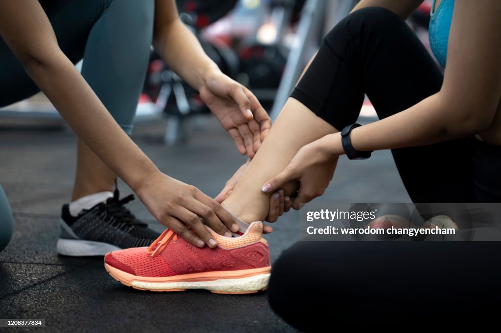 Sports women with personal trainer in gym. Sports woman having injury ankle.