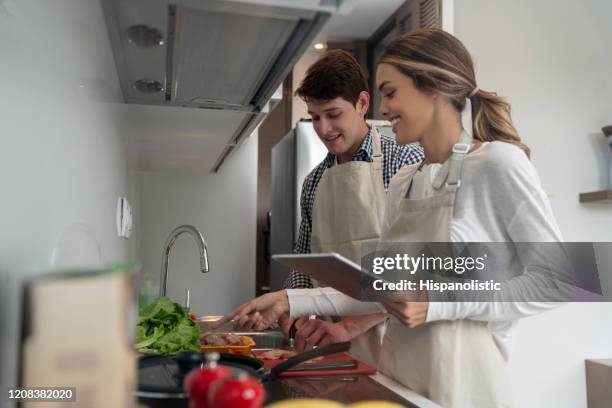 young latin american couple cooking together at home using an online recipe having fun - following recipe stock pictures, royalty-free photos & images