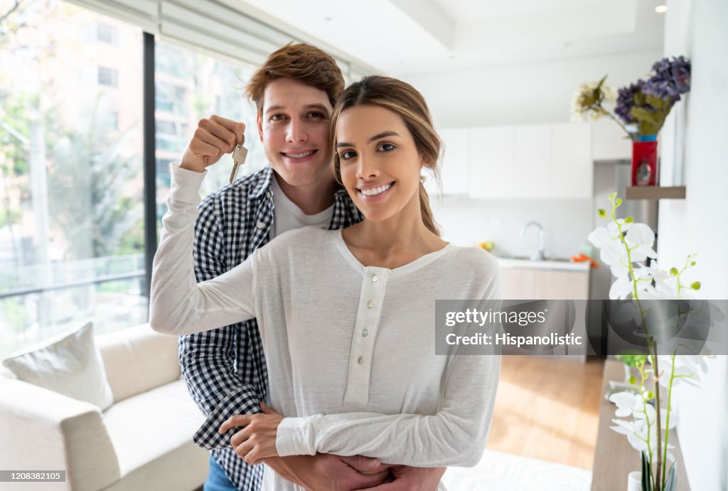 Beautiful young couple at their new home holding the keys looking at camera smiling