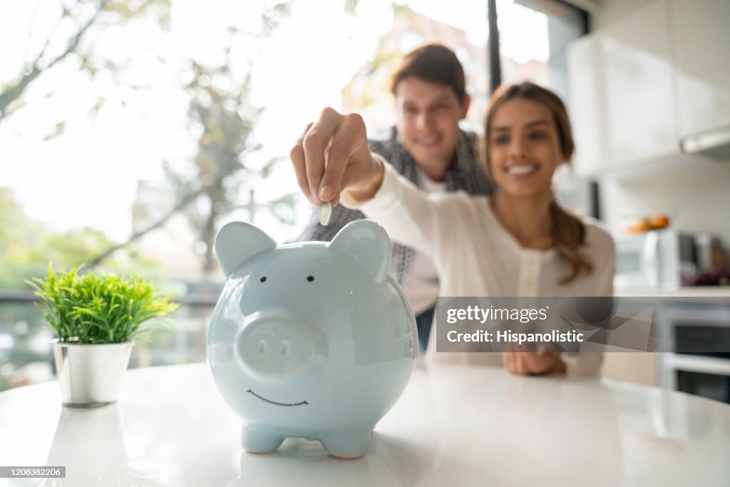 Focus on foreground of latin american young couple saving coins into piggy bank