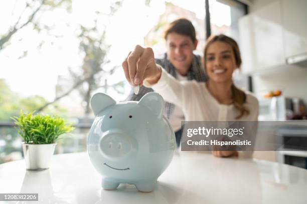 focus on foreground of latin american young couple saving coins into piggy bank - savings stock pictures, royalty-free photos & images