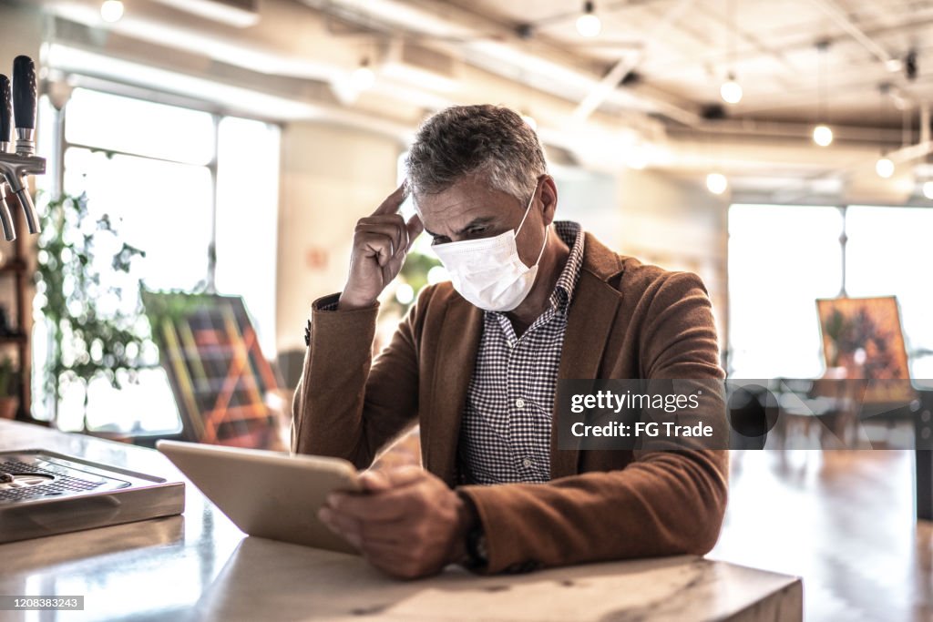 Mature businessman with mask using digital tablet at work