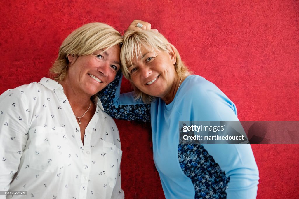 Retrato de parejas maduras de mujeres LGBTQ posando en pared roja.