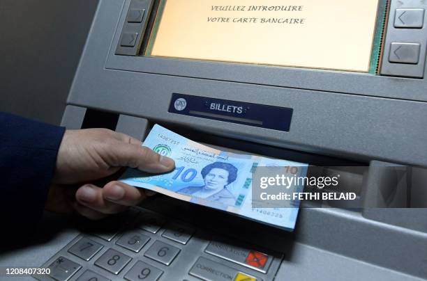 Man retrieves newly circulating Tunisian bank notes from an ATM in the capital Tunis, on March 27, 2020. - The Central Bank of Tunisia today put new...