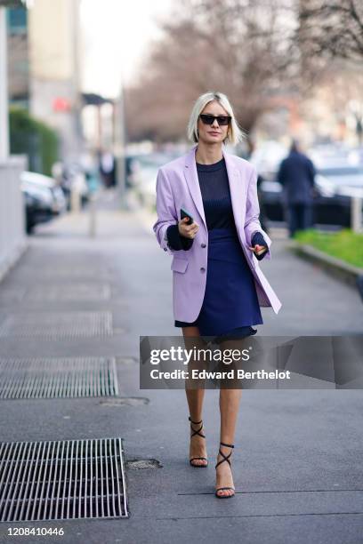 Lisa Hahnbueck wears sunglasses, a pale purple oversized long blazer jacket, a blue dress with a mesh part, shoes, outside BOSS, during Milan Fashion...