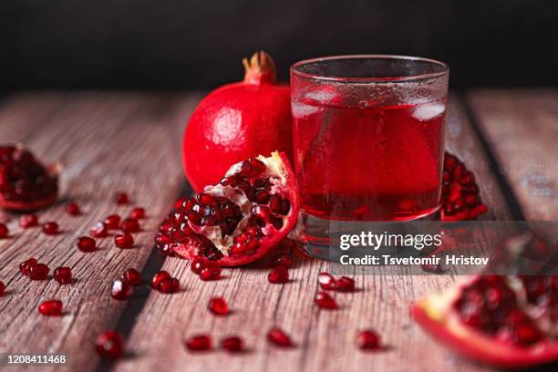 juice of pomegranate in glass. half pomegranate and ripe pomegranate fruit with seeds on rustic wood background. - granaatappel stockfoto's en -beelden