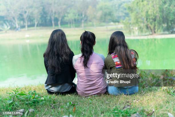 young girls are sitting near the lake and enjoying the nature - three people sitting stock pictures, royalty-free photos & images