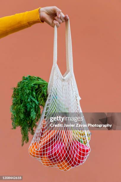 woman holding reusable cotton mesh bag with fruit and vegetables - frugality stock pictures, royalty-free photos & images