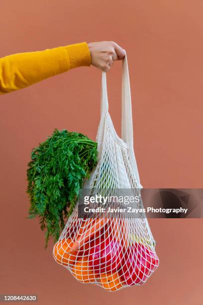 woman holding reusable cotton mesh bag with fruit and vegetables - tote bag fotografías e imágenes de stock